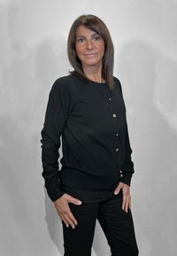 Cardigan nero con maniche lunghe, scollo rotondo e bottoni dorati sul davanti. Indossato sopra pantaloni neri. Tessuto liscio.
