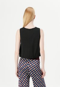 Mouwloos zwart topje met een ronde halslijn en een kleine rits aan de achterkant, gecombineerd met patroonrijke wijde broek met geometrische ontwerpen in blauw en bordeauxrood.