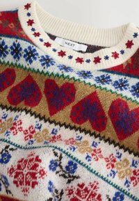 Pull en maille crème avec des cœurs rouges, des flocons de neige bleus et rouges, et des motifs floraux, présentant un col côtelé brodé de fleurs rouges et bleues.