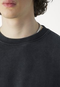 Černá bavlněná mikina s kulatým výstřihem, žebrovanými rukávy a měkkou texturou, zdobená vrstveným stříbrným a perlovým náhrdelníkem.