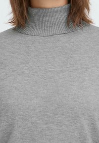 Hellgrauer Rollkragenpullover mit einem gerippten hohen Kragen, weicher Textur und einem schlichten, eleganten Design. Keine sichtbaren Muster oder Akzente.