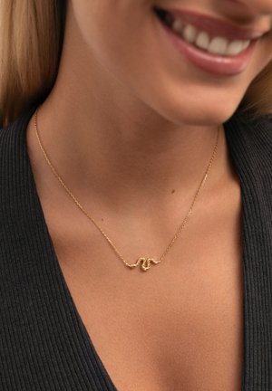 Collarín en forma de serpiente de oro sobre una delicada cadena, con un diseño retorcido y acentos texturizados, llevado sobre una blusa de canalé oscura.