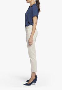 Námořnická modrá blůza s krátkým rukávem, béžové úzké kalhoty a námořnické semišové lodičky na vysokém podpatku, zobrazené z boku.