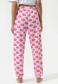 Roze pyjamabroek met een herhaald patroon van rode lippen. Gemaakt van zachte stof met een elastische tailleband en taps toelopende boorden.