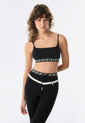 Black crop top with thin straps and a contrasting patterned band. High-waisted black leggings with white accents and an adjustable drawstring.