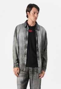 Spijkerblouse in grijs verloop met knoopsluiting, gecombineerd met een zwarte t-shirt met een rood grafisch logo, getoond met bijpassende broek.