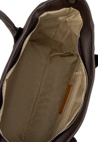 Interno di una borsa in pelle marrone, con una fodera in tessuto beige chiaro, una tasca con cerniera su un lato e trame lisce in tutto.