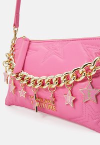 Růžová prošívaná kabelka na rameno s zlatým řetízkem, hvězdnými přívěsky a detailem s logem. Materiál vypadá hladce a synteticky.