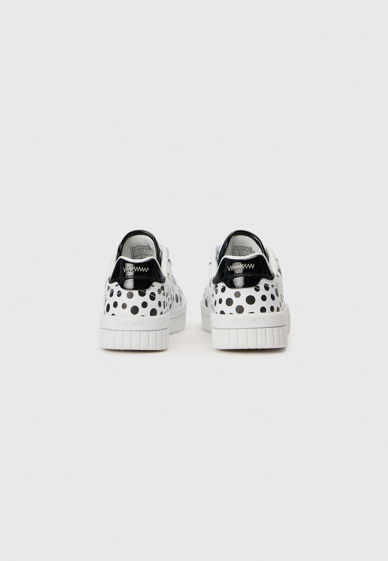 Une paire de baskets Skechers blanches avec des pois noirs et des accents de talon noir brillant, montrée de dos sur un fond blanc.