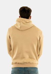 Sudadera color crema con un ajuste relajado, que presenta una gran capucha y una textura suave. La vista trasera muestra el dobladillo redondeado y las costuras mínimas.
