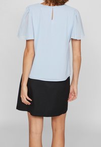 Top azzurro chiaro con maniche trasparenti a sbuffo e un dettaglio a chiave sul retro, abbinato a una gonna nera che presenta una texture liscia.