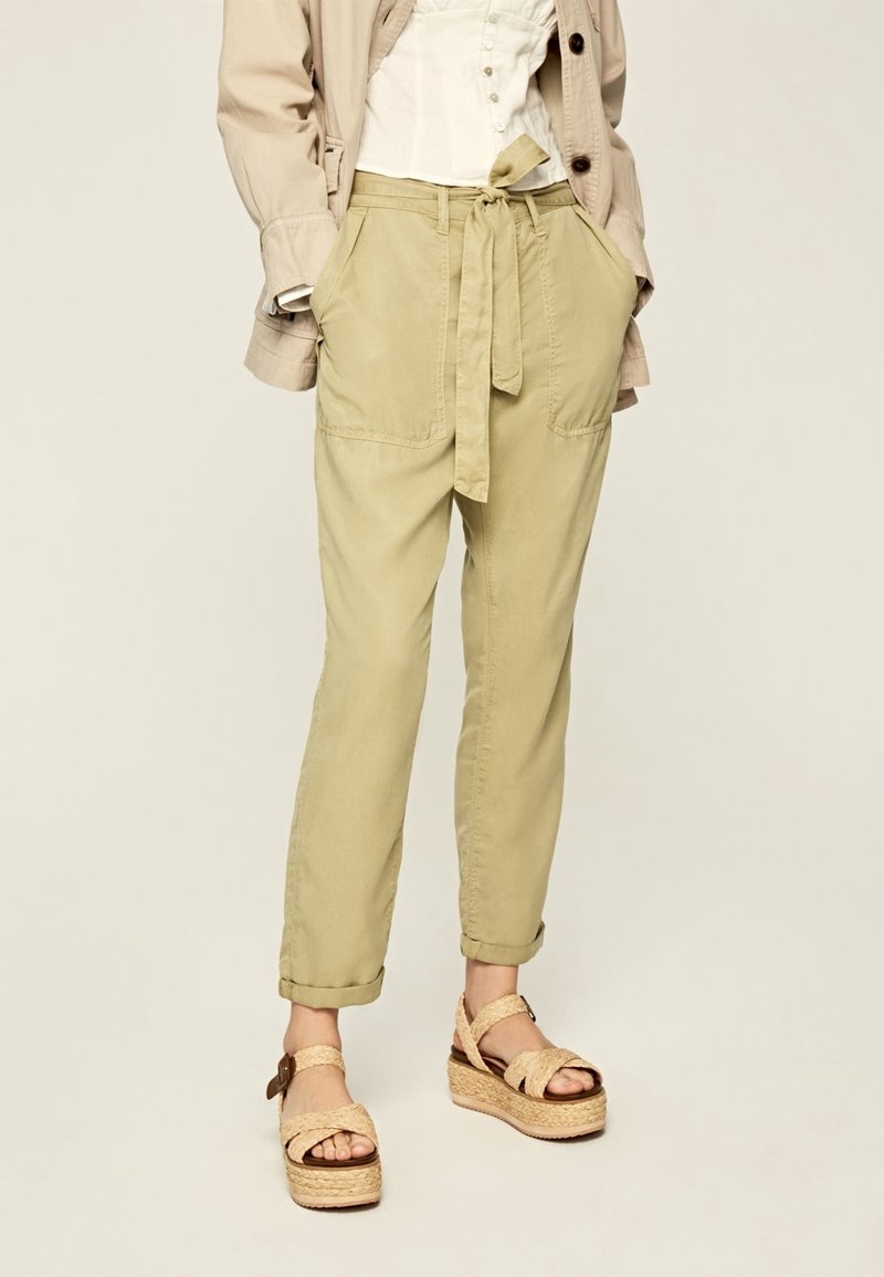 Pantaloni beige con cintura a fascia, due tasche frontali, risvolti e un fit rilassato. Abbinati a sandali platform color cuoio con dettagli intrecciati.