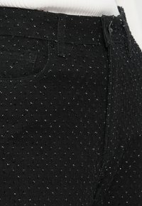 Jeans de ganga pretos com uma superfície texturizada com pequenos pontos em relevo, cinco bolsos e fecho de correr. Um brilho subtil acrescenta detalhe.