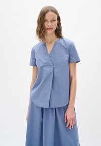 Maglietta azzurro chiaro a maniche corte con scollatura a V e dettaglio di piega frontale. Realizzata in un tessuto morbido, presenta un corpetto aderente e un orlo curvo.