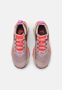 Chaussures de sport avec un design beige clair et brun rougeâtre, tige en mesh, lacets roses, semelle texturée et accents orange vif.