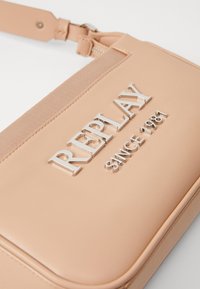 Ροζ δερμάτινη τσάντα με λείο υφή, διαθέτει μεταλλικό λογότυπο "REPLAY" και την ένδειξη "SINCE 1981" ανάγλυφα στο μπροστινό μέρος. Κλείσιμο με φερμουάρ και λουράκι.