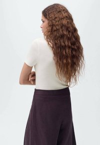 Off-white kortemouw top gemaakt van een gladde brei-stof, gecombineerd met hooggesneden donkere broek. Model heeft lang, golvend haar.