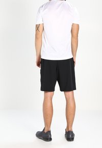 Weißes kurzärmliges Sportshirt kombiniert mit schwarzen Shorts, mit einem klaren Design und glattem Stoff. Trägt dazu schwarze Sportschuhe.