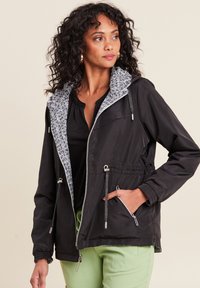 Schwarze Jacke mit einer gemusterten grauen Kapuze, vorderem Reißverschluss, verstellbarem Bund und seitlichen Taschen. Glatte Textur, leichtes Material.