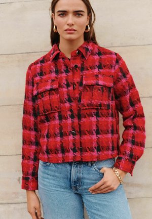 Rood en roze gecheckte cropped jas met zwarte accenten, voorzien van twee borstzakken en zwarte knopen, gecombineerd met lichtblauwe jeans.