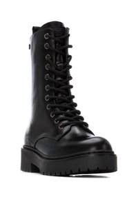 Bota de cuero negro con cordones, de caña alta, suela gruesa, herrajes plateados en los ojetes y un acabado suave. Patrón de relieve resistente en la suela.