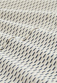Lichtgekleurde stof met een ruitpatroon van marineblauwe en witte rechthoekige vormen. De textuur lijkt glad en zacht te zijn.