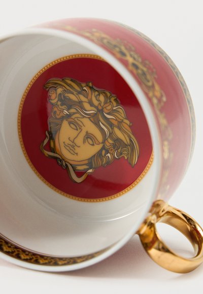 Tasse en porcelaine blanche avec poignée en or, intérieur de base rouge présentant un motif détaillé de tête de Méduse, et motifs dorés ornés sur le bord.