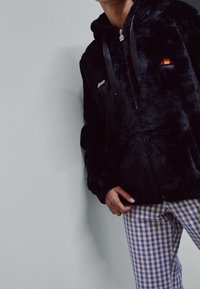 Sort fleece hoodie med lynlås og satin snore, der har et lille broderet logo og et accentdesign på brystet.