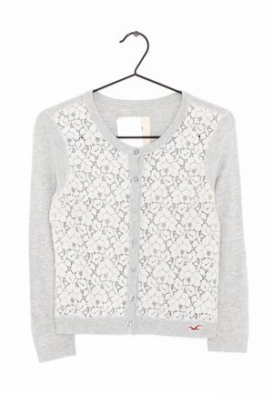 Jasnoszara kardigan z koronkowym panelem z przodu w kwiatowy wzór, szarym dzianinowym rękawem i pięcioma guzikami. Mały detal z logo blisko dołu.