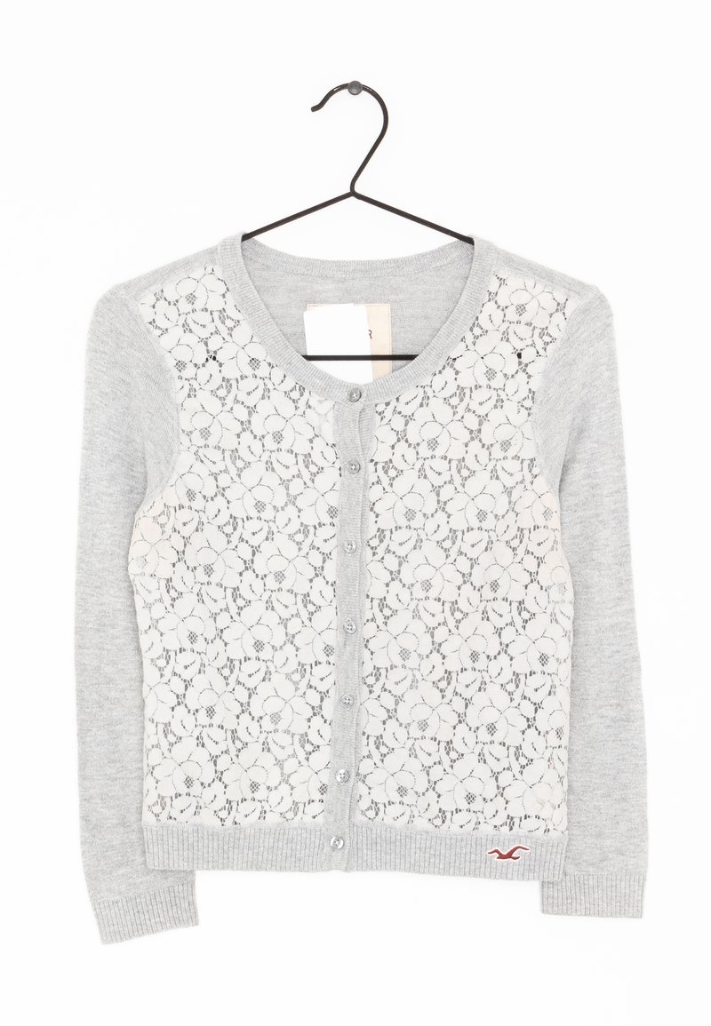Ljusgrå cardigan med spetsframpanel och blommönster, grå stickade ärmar och fem knappar. Liten logotypdetalj nära nederkanten.