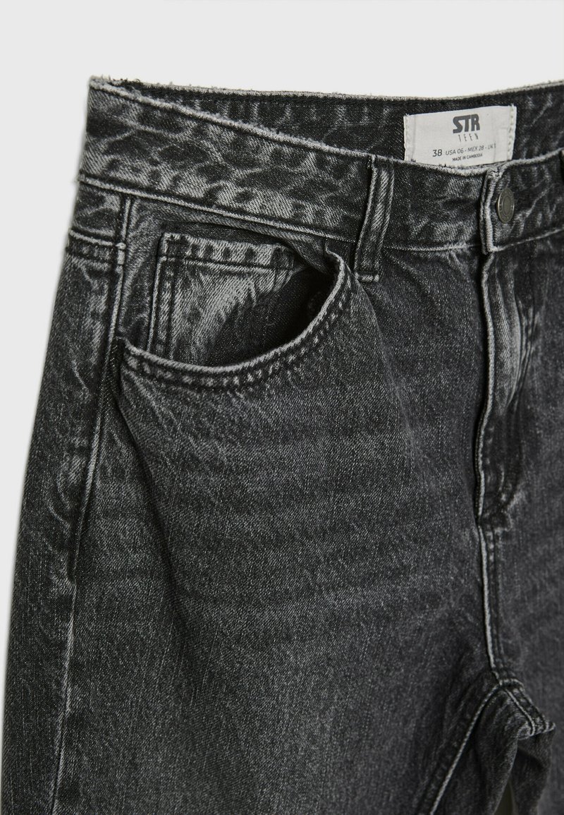 Jeans in denim nero con una finitura testurizzata, caratterizzati da una tasca frontale angolata, cuciture a contrasto e un'etichetta cucita nella cintura.