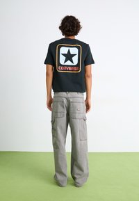 Black cotton t-shirt with a large white star logo and retro "CONVERSE" text on the back, paired with gray cargo pants featuring multiple pockets.