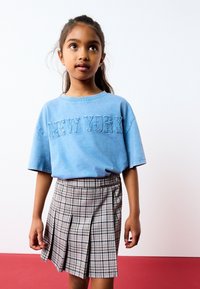 Jasnoniebieska koszulka z krótkim rękawem z białym napisem "NEW YORK", w komplecie z plisowaną spódnicą w kratkę w odcieniach szarości, czerni i pastelowych kolorach.