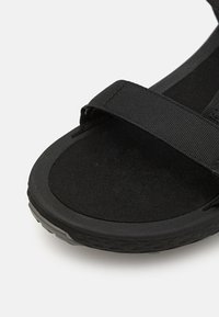 Black sandal featuring a soft textured footbed, adjustable fabric straps, and a rubber outsole with a patterned tread for grip.