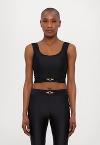 Top corto aderente nero con spalline larghe, caratterizzato da un accento circolare dorato in vita. Texture liscia e design snello, abbinato a pantaloni neri coordinati.