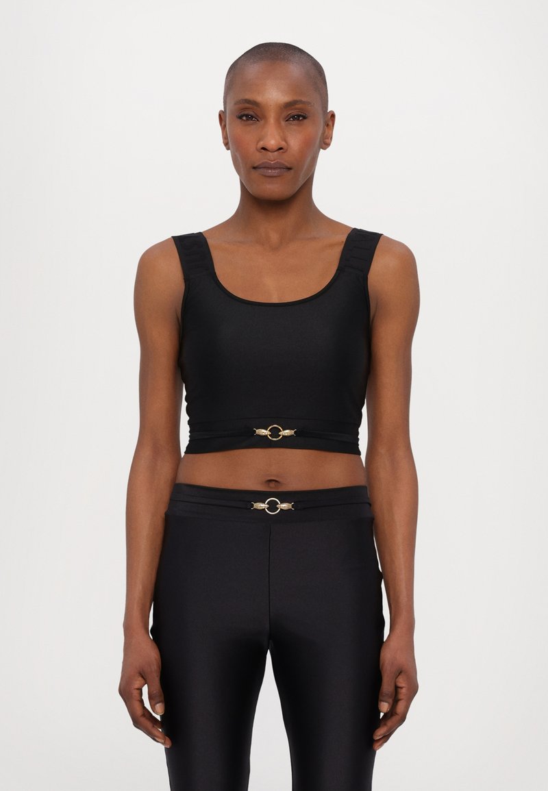 Top corto aderente nero con spalline larghe, caratterizzato da un accento circolare dorato in vita. Texture liscia e design snello, abbinato a pantaloni neri coordinati.