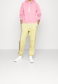 Rosa hoodie med framficka och dragsko, kombinerad med gula joggers. Vita sneakers fulländar outfiten. Enkel, avslappnad design.