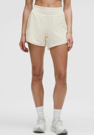Cream-colored athletic shorts with a stretchy waistband and side pockets. The fabric appears smooth and lightweight, suitable for active wear.