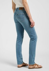 Jeans de denim azul ajustados con un lavado claro, que cuentan con una etiqueta de cuero marrón en la parte trasera de la cintura y un diseño clásico de cinco bolsillos.
