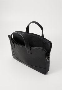 Black leather bag with a textured finish, dual handles, a zip closure, and a flat base. Features an external pocket and subtle brand logo.