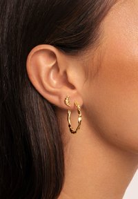 Gold hoop earrings featuring a textured, irregular design. One earring is smaller with a twisted accent, highlighting unique shapes.