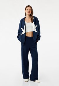 Sudadera azul marino con un diseño de estrella blanca, combinada con pantalones de chándal azul marino. Tejido de algodón, corte holgado y textura acanalada en la parte superior corta.