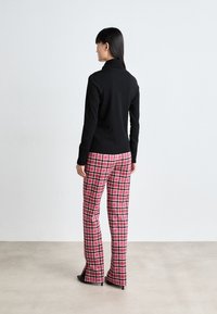 Pull en tricot noir avec col haut, associé à un pantalon à motif pied-de-poule rose avec des accents noir et blanc et des bas de jambes évasés.