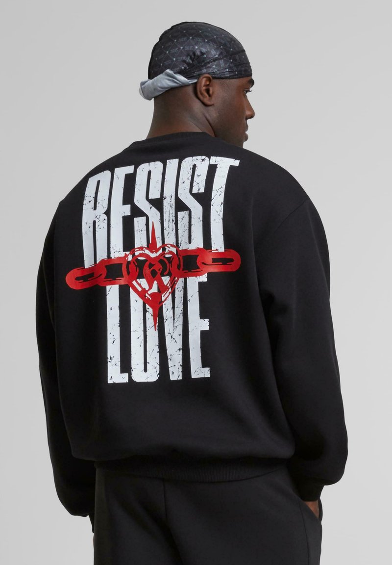 Black sweatshirt featuring large white text "RESIST" and "LOVE" with a red heart and chain graphic on the back; crew neck and relaxed fit.