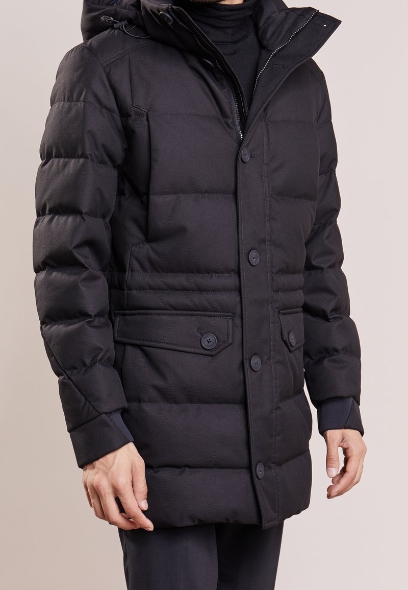 Svart puffjacka med huva, med en texturerad utsida, tryckknappar, sidofickor och ribbade muddar för extra värme.