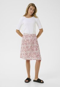 Weißes geripptes Shirt mit Drei-Viertel-Ärmeln und einem Rock mit pinkem Blumenmuster. Der Rock hat einen elastischen Bund und ist knielang. Schwarze Sandalen.