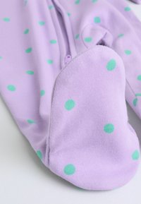 Pyjama bébé lavande avec pieds et pois verts, montrant un gros plan de la zone du pied et de la texture du tissu.
