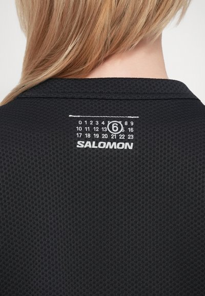 Zwart textiel shirt met een kraag, voorzien van een wit genummerd label en het "SALOMON" logo op de achterkant van de nek.