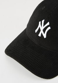Casquette en velours côtelé noire avec un logo "NY" entrelacé blanc brodé à l'avant, inclinée sur un fond blanc.