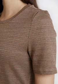 Haut à manches courtes avec un motif géométrique marron, beige et noir ; tissu texturé ; encolure ronde avec une bordure subtile.